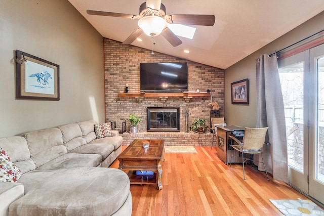 living area featuring light wood finished floors, ceiling fan, a fireplace, and vaulted ceiling