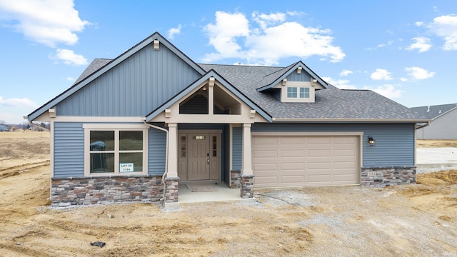 craftsman-style home with dirt driveway, stone siding, roof with shingles, and an attached garage