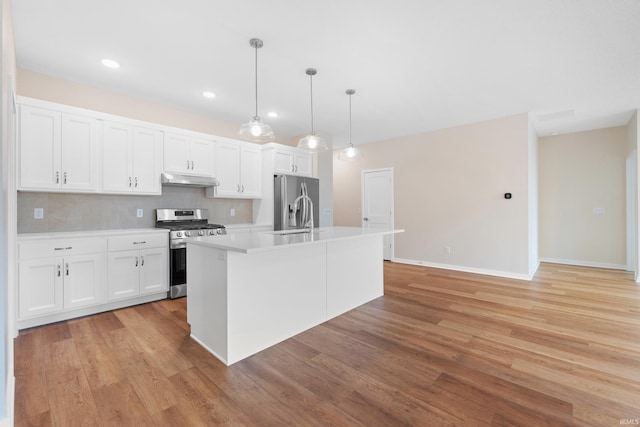 kitchen featuring white cabinets, appliances with stainless steel finishes, decorative light fixtures, a kitchen island with sink, and under cabinet range hood