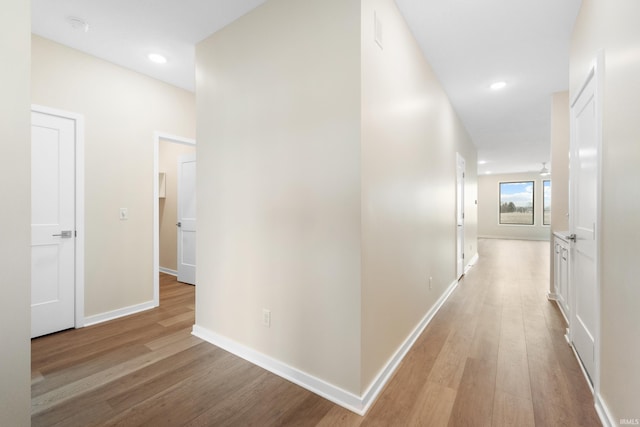 hallway featuring light wood finished floors, baseboards, and recessed lighting