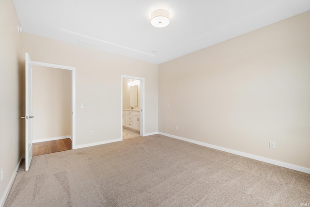 unfurnished bedroom featuring light carpet, baseboards, and ensuite bathroom