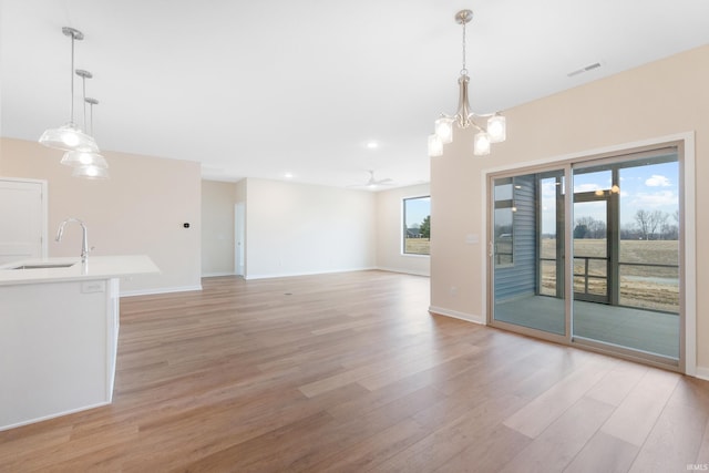 interior space featuring ceiling fan with notable chandelier, a sink, visible vents, baseboards, and light wood-type flooring