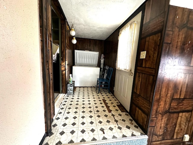 hallway with light floors, wooden walls, a textured ceiling, and a textured wall