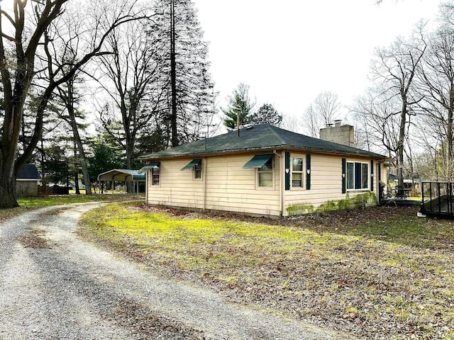 view of side of home with a chimney, gravel driveway, and a detached carport