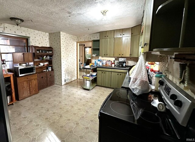 kitchen featuring a textured ceiling, stainless steel microwave, dark countertops, and wallpapered walls