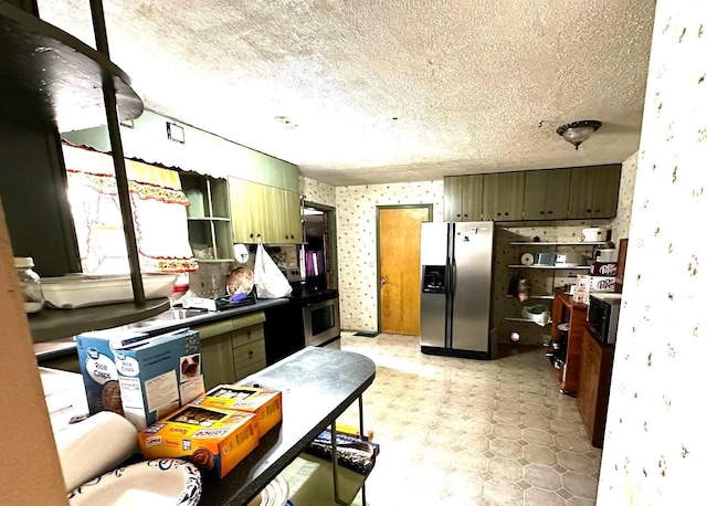 kitchen with wallpapered walls, a textured ceiling, appliances with stainless steel finishes, and green cabinetry