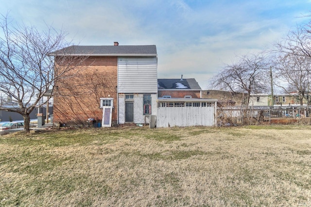 rear view of house with brick siding, a yard, a chimney, and fence