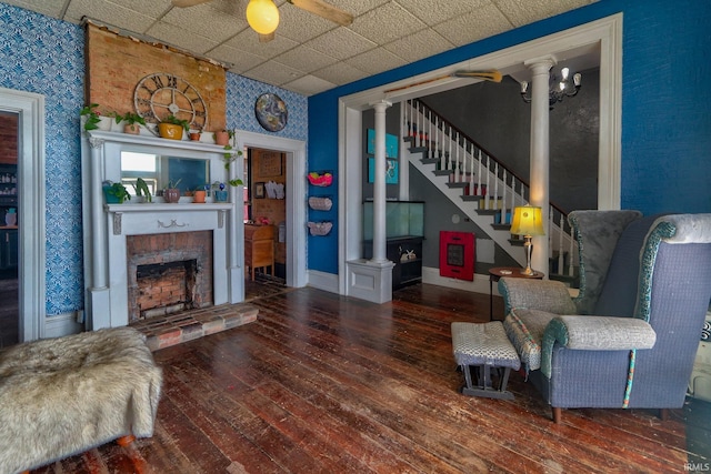 living area with a brick fireplace, stairway, dark wood-style flooring, and ornate columns