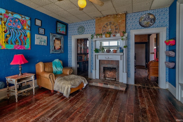 living area featuring a drop ceiling, a fireplace, wood finished floors, and wallpapered walls