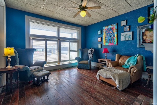 living area featuring a textured wall, a paneled ceiling, wood finished floors, and a ceiling fan