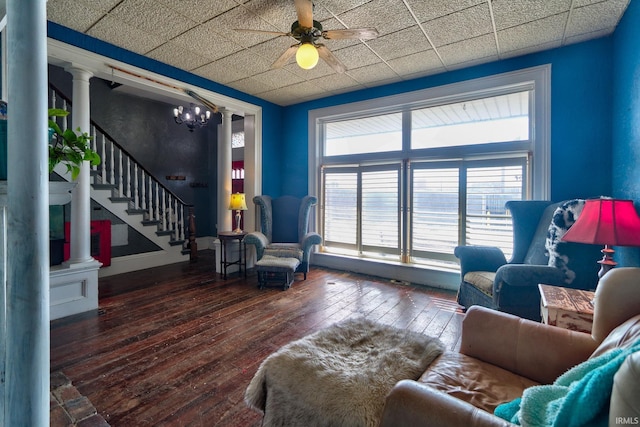 living area with decorative columns, a drop ceiling, a ceiling fan, dark wood-style floors, and stairway