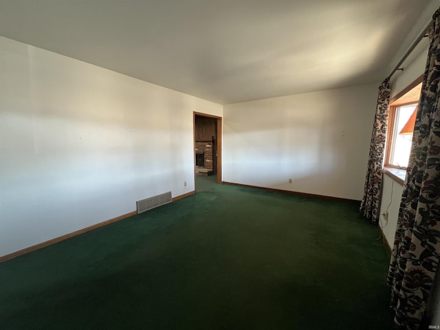 unfurnished room featuring a fireplace with raised hearth, dark colored carpet, visible vents, and baseboards