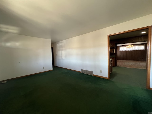 empty room with a chandelier, dark colored carpet, visible vents, and baseboards