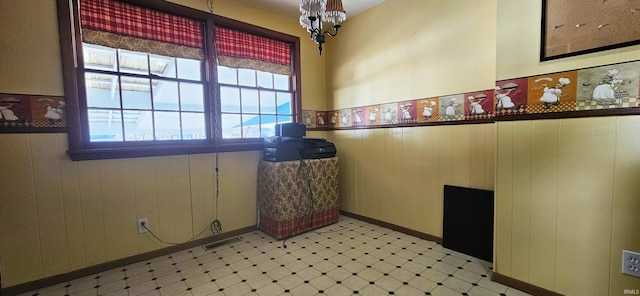 interior space with visible vents, wainscoting, wood walls, light floors, and a chandelier