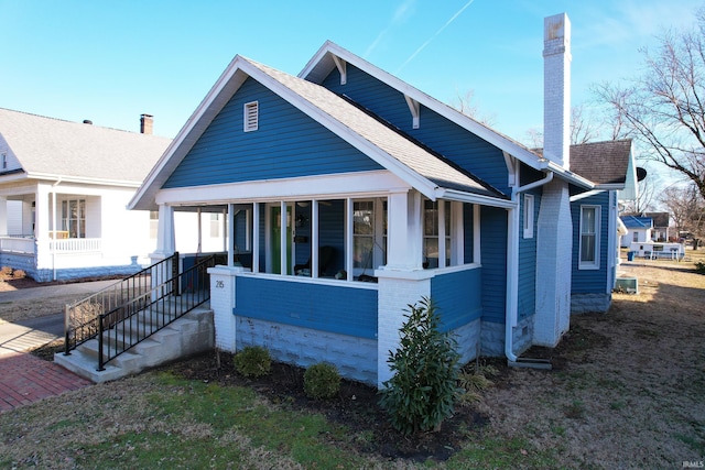 bungalow-style house with a shingled roof, a chimney, a porch, and brick siding