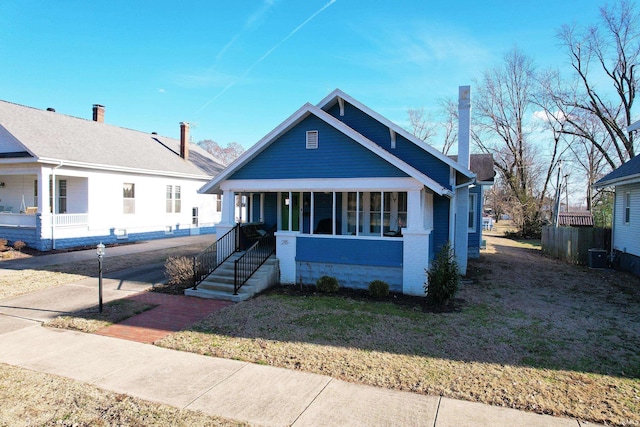 bungalow-style home featuring a chimney, covered porch, fence, cooling unit, and a front lawn