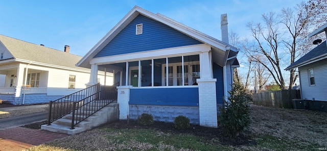 bungalow-style house with brick siding, a chimney, fence, and a sunroom