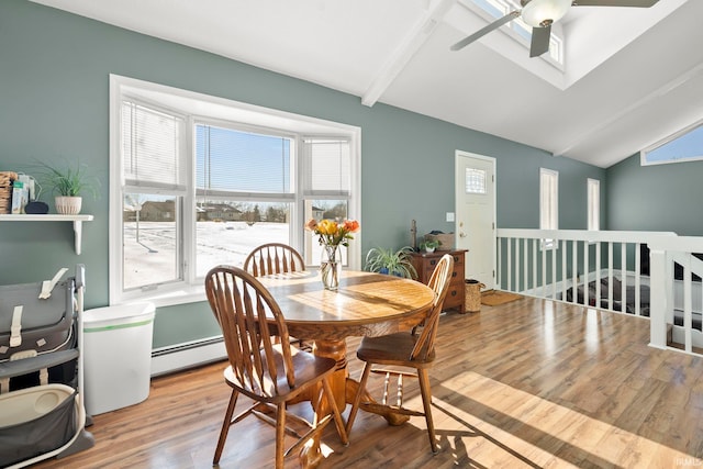 dining room with lofted ceiling with skylight, a healthy amount of sunlight, baseboard heating, and wood finished floors