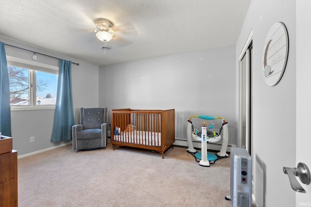 carpeted bedroom featuring a closet, a baseboard heating unit, a textured ceiling, a crib, and baseboards