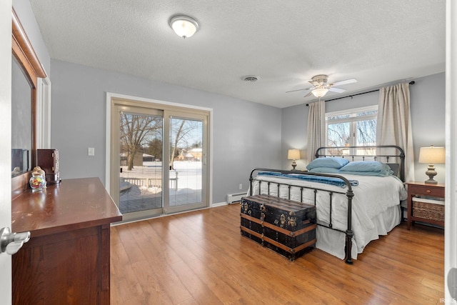 bedroom with a textured ceiling, a baseboard radiator, light wood-style flooring, visible vents, and access to exterior