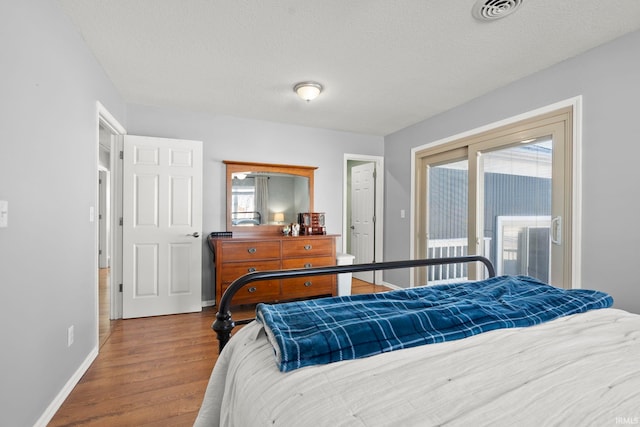 bedroom featuring baseboards, a textured ceiling, visible vents, and wood finished floors