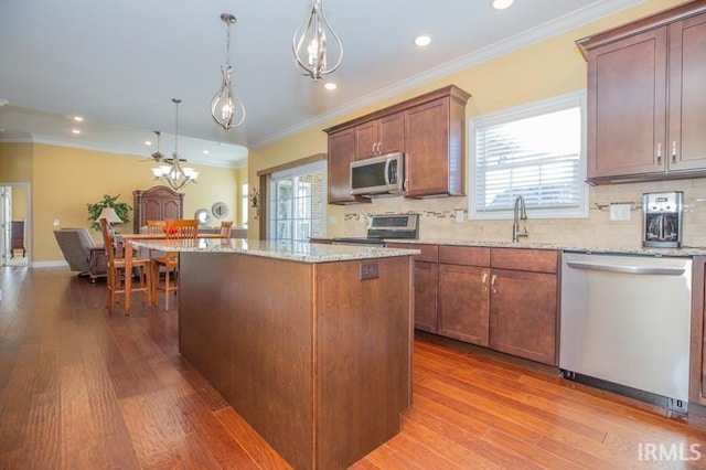 kitchen featuring appliances with stainless steel finishes, crown molding, a kitchen island, and wood finished floors