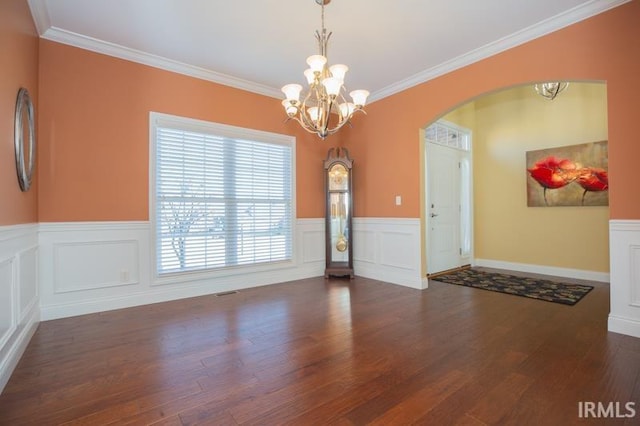 unfurnished dining area featuring arched walkways, a chandelier, wood finished floors, ornamental molding, and wainscoting