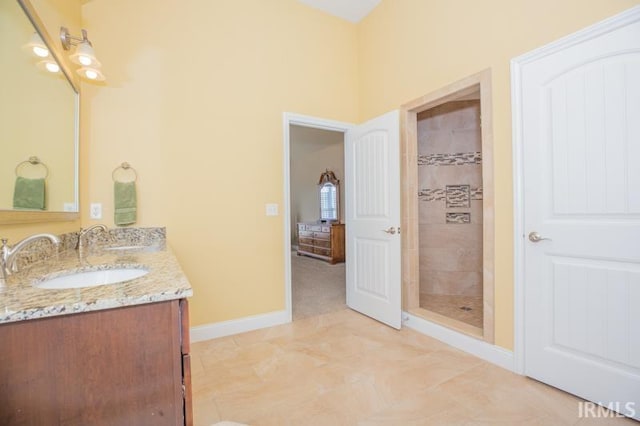 full bath with a tile shower, double vanity, a sink, and baseboards