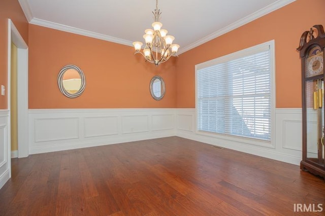 empty room with a wainscoted wall, an inviting chandelier, wood finished floors, and crown molding