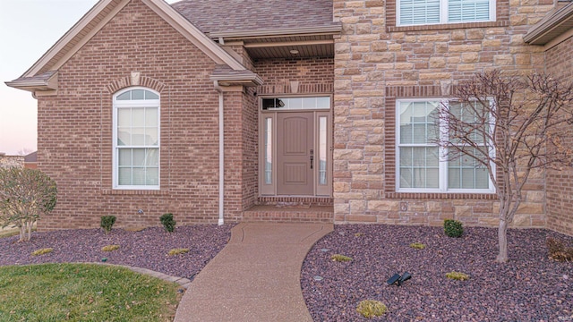 entrance to property with a shingled roof, stone siding, and brick siding