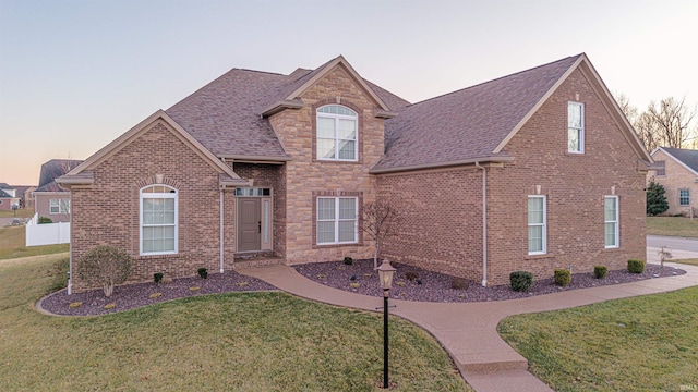 traditional-style home featuring a shingled roof, brick siding, and a front lawn