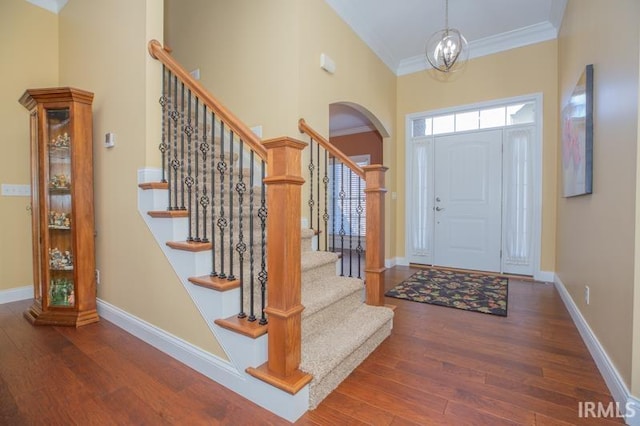 entryway featuring arched walkways, crown molding, a towering ceiling, wood finished floors, and baseboards