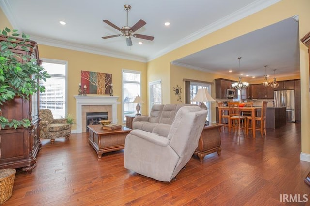 living area featuring dark wood-style floors, a fireplace, recessed lighting, ornamental molding, and ceiling fan with notable chandelier