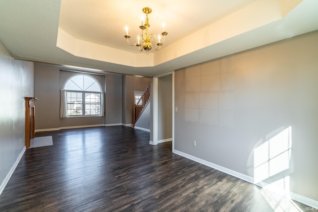 unfurnished room featuring a chandelier, baseboards, stairway, a tray ceiling, and dark wood finished floors