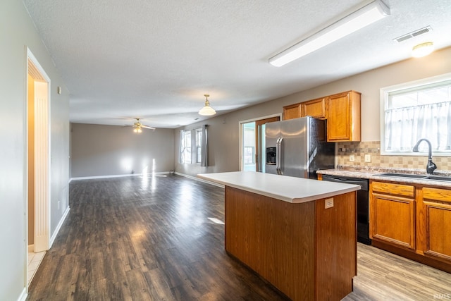 kitchen featuring visible vents, a kitchen island, open floor plan, stainless steel refrigerator with ice dispenser, and a sink