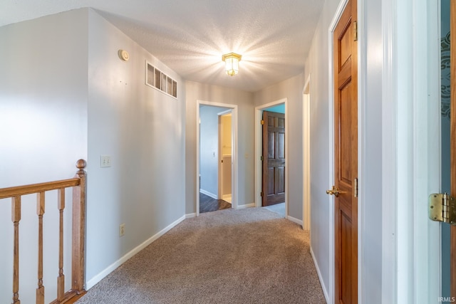 corridor featuring baseboards, visible vents, an upstairs landing, a textured ceiling, and carpet flooring