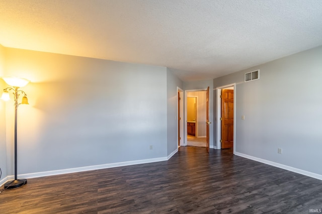 spare room featuring baseboards, a textured ceiling, visible vents, and dark wood-type flooring