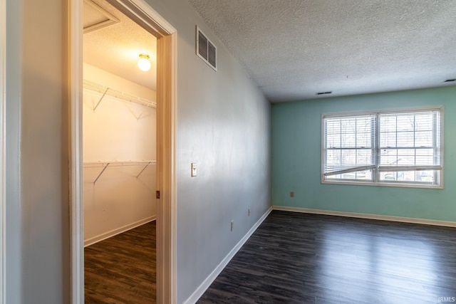 unfurnished room with dark wood-style floors, baseboards, visible vents, and a textured ceiling