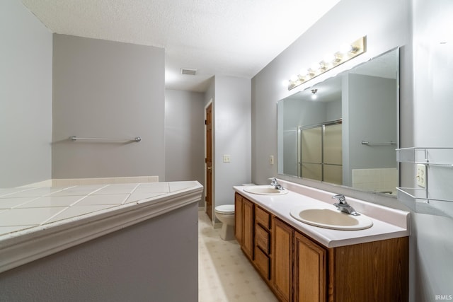 full bath with a textured ceiling, double vanity, a sink, and toilet