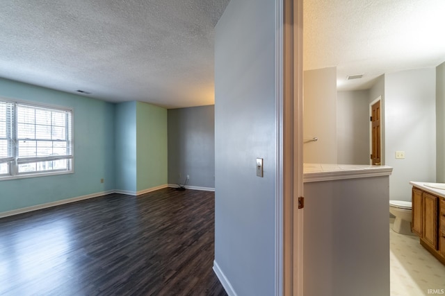 corridor with visible vents, a textured ceiling, baseboards, and wood finished floors