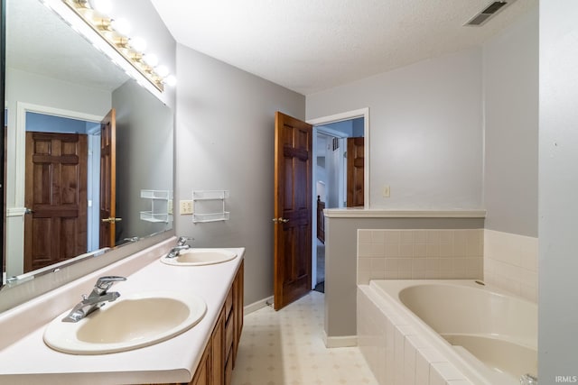 full bath featuring a bath, a textured ceiling, a sink, and visible vents