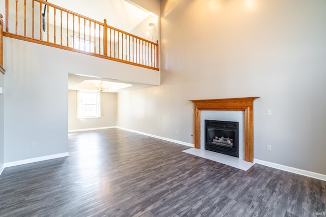 unfurnished living room with dark wood-style flooring, an inviting chandelier, a fireplace with flush hearth, and baseboards