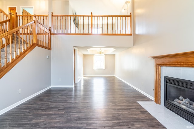 unfurnished living room with a tile fireplace, baseboards, stairs, dark wood finished floors, and an inviting chandelier