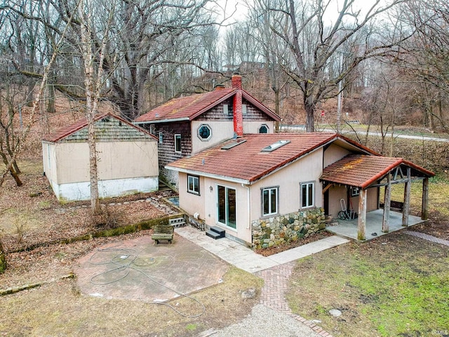 back of house with a patio, stone siding, a tile roof, a chimney, and stucco siding