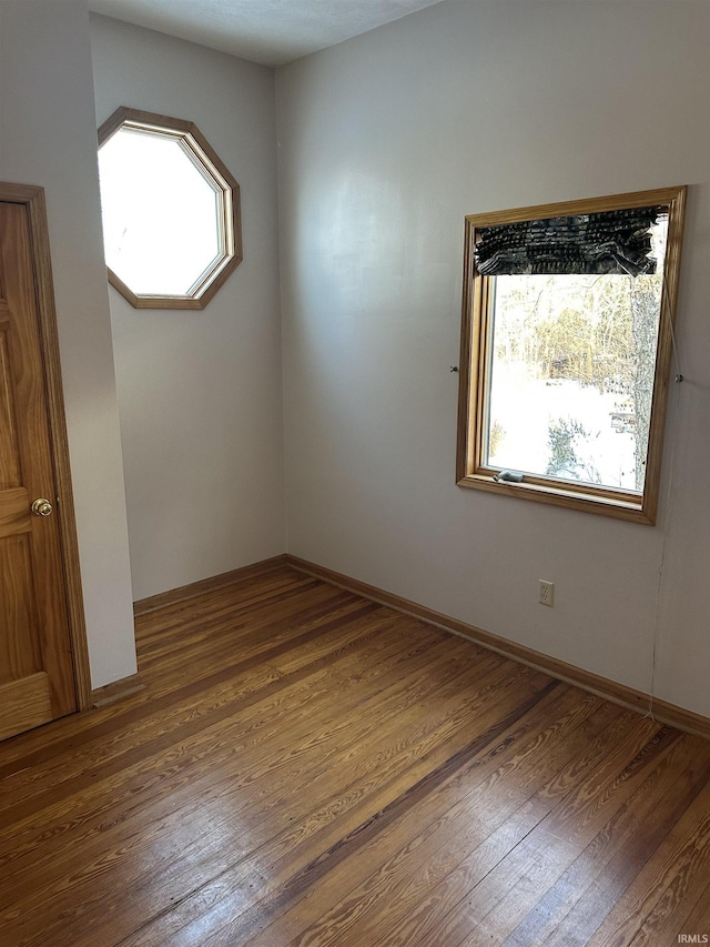 unfurnished room featuring a healthy amount of sunlight, baseboards, and wood finished floors