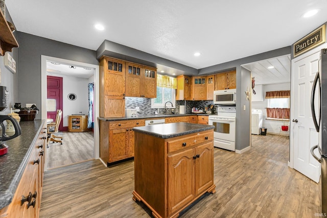 kitchen featuring dark countertops, brown cabinetry, glass insert cabinets, a kitchen island, and white appliances