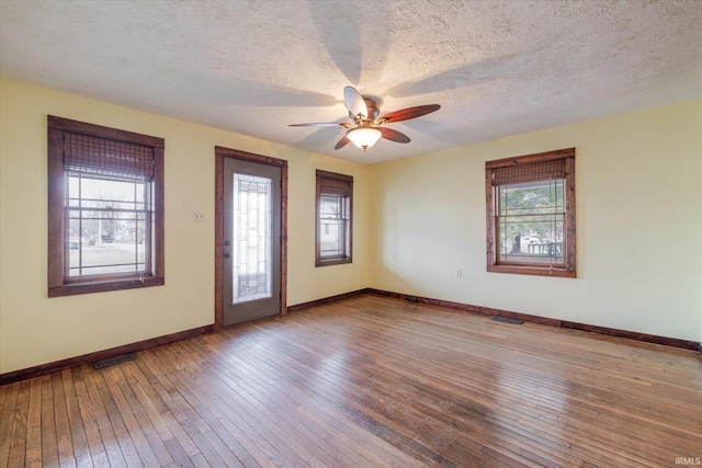 empty room with a textured ceiling, hardwood / wood-style flooring, visible vents, a ceiling fan, and baseboards