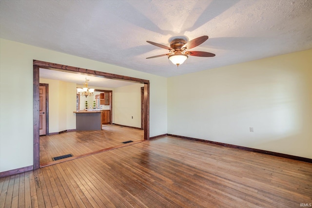 unfurnished room featuring wood-type flooring, visible vents, a textured ceiling, and baseboards