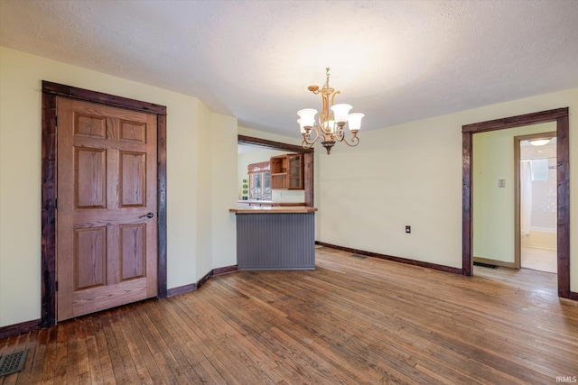 interior space featuring dark wood-style floors, visible vents, a textured ceiling, a chandelier, and baseboards