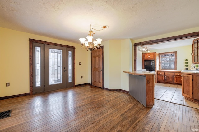 entrance foyer with a notable chandelier, visible vents, a textured ceiling, baseboards, and hardwood / wood-style flooring